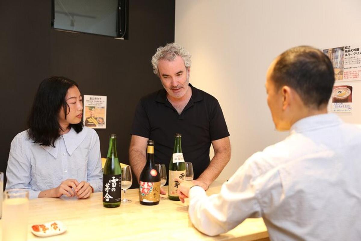 tre persone sedute attorno a un tavolo con bottiglie di vino