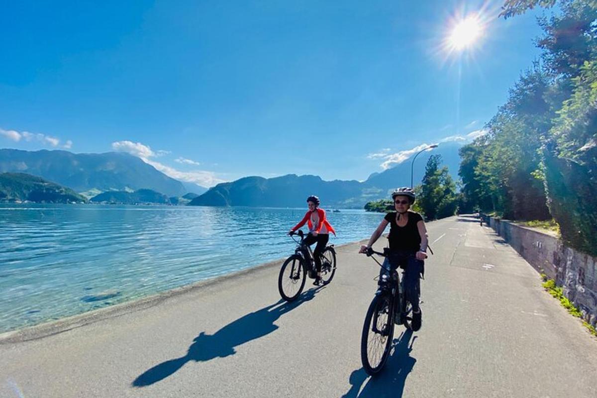 two people riding bikes down a road next to a lake