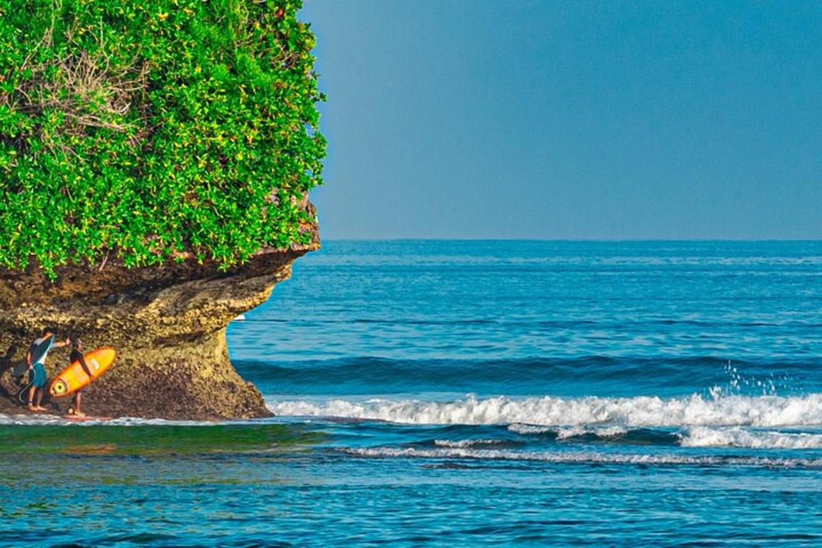 a person with a surfboard sitting on a cliff next to the ocean