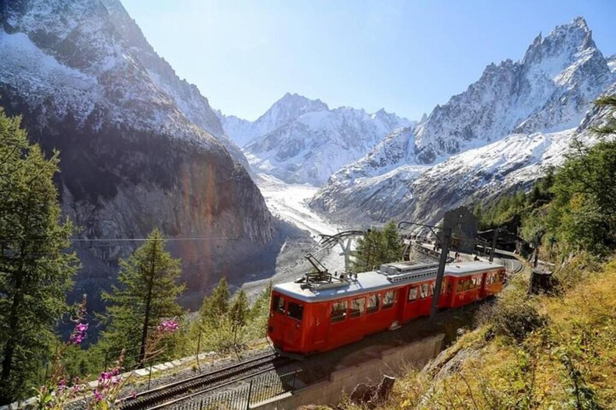 Un tren rojo que viaja por las vías en las montañas.