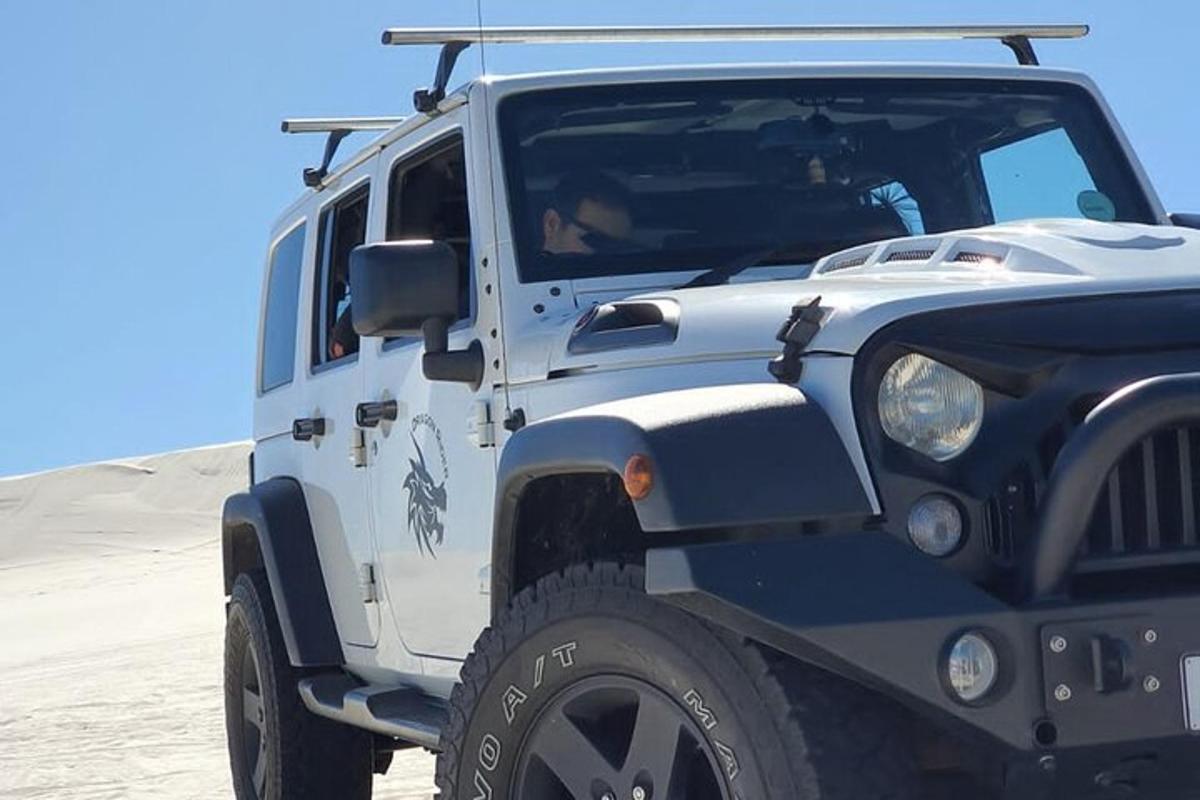 ein weiß-schwarzer Jeep, der im Sand geparkt ist