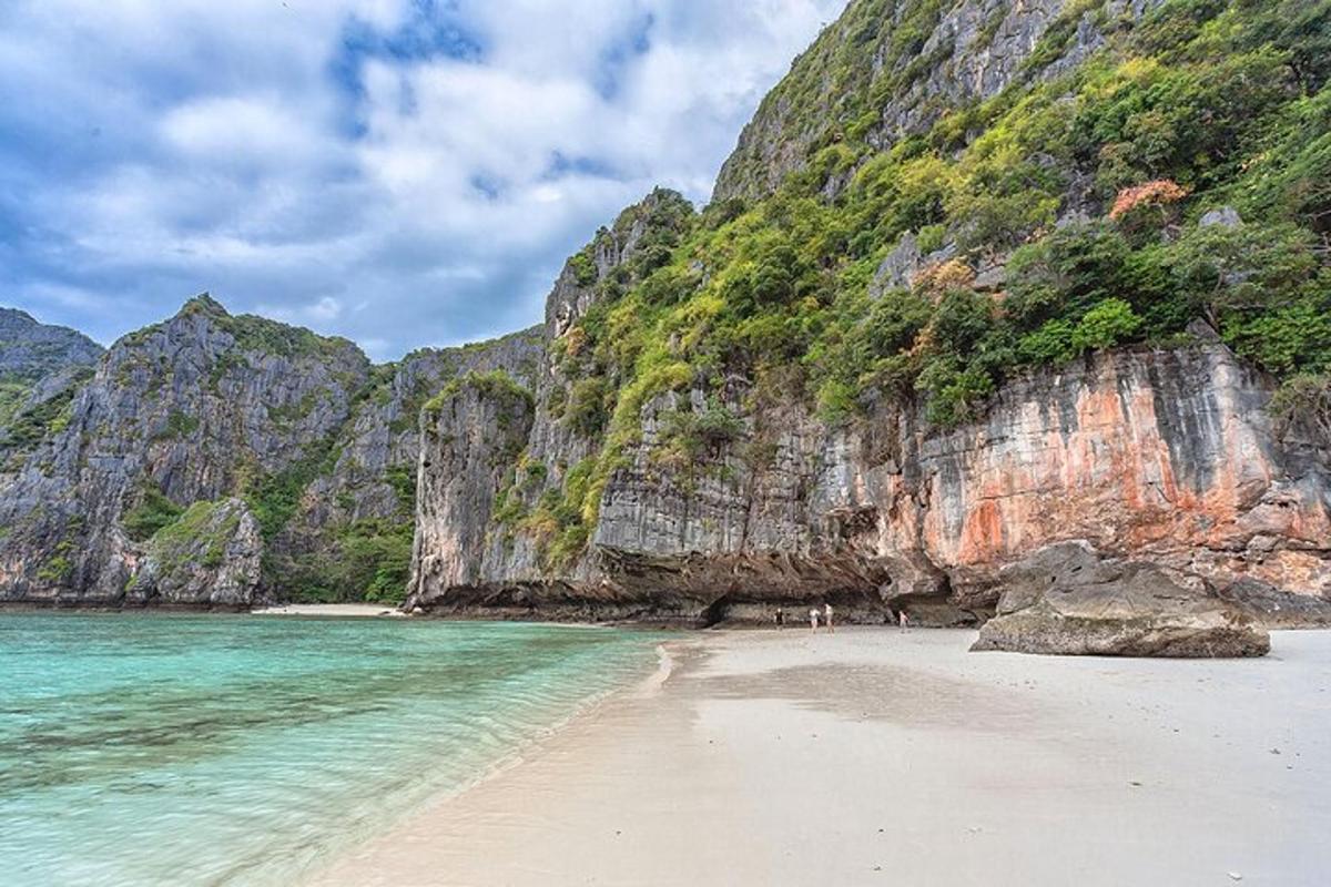 a beach with people standing on the sand next to a mountain