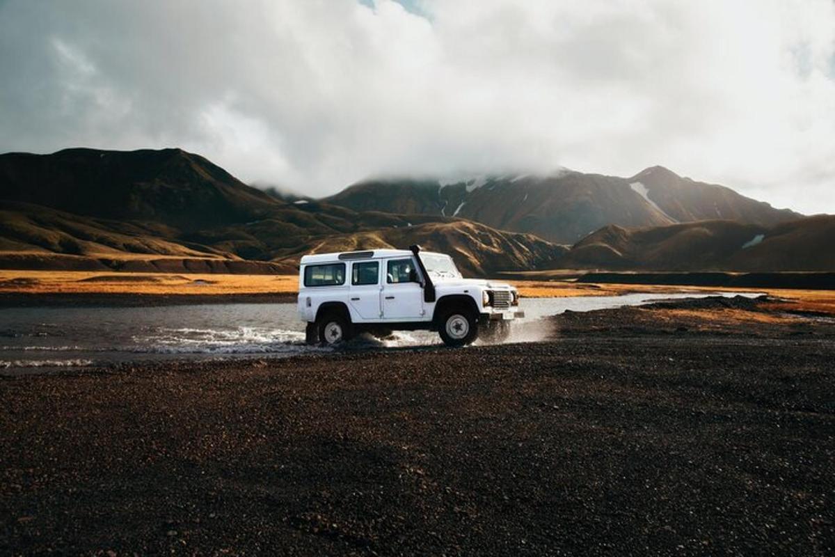 una jeep bianca che attraversa un fiume con montagne