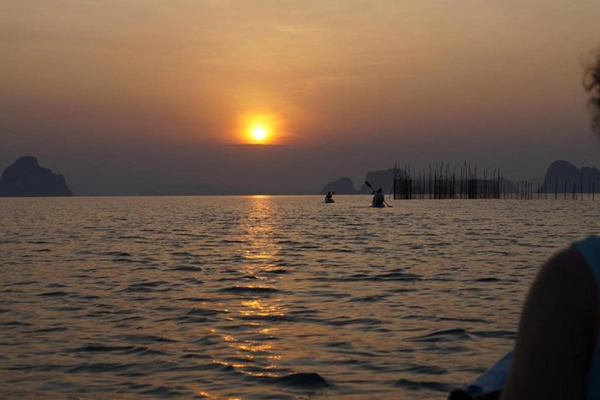 duas pessoas em barcos na água ao pôr do sol