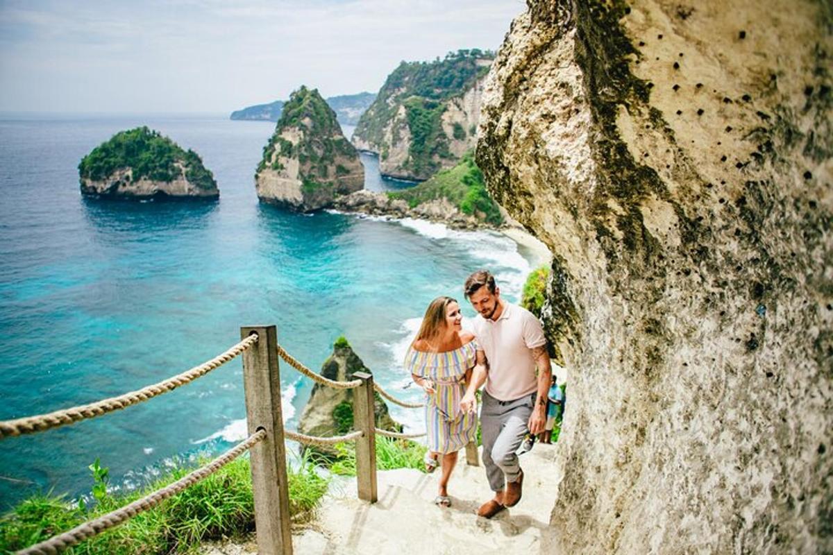 Un hombre y una mujer caminando por un acantilado con vistas al océano.