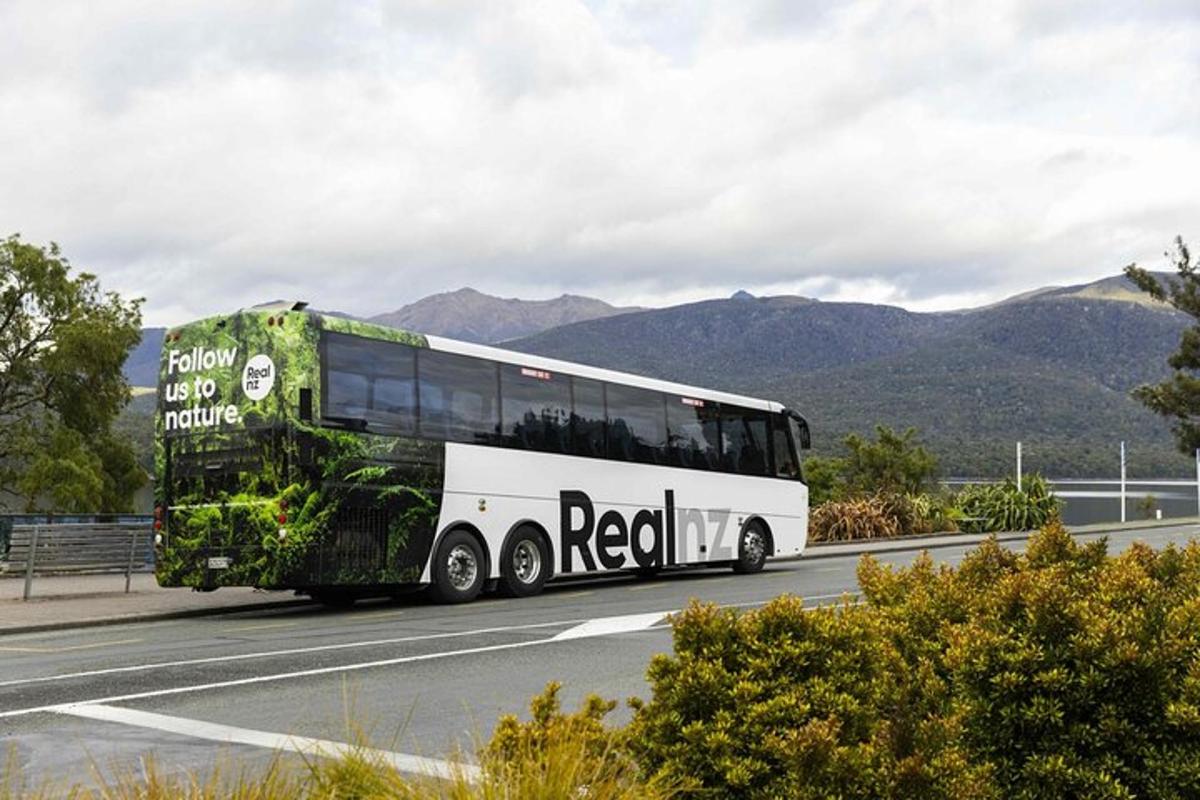 Un autobús circulando por una carretera con montañas al fondo.