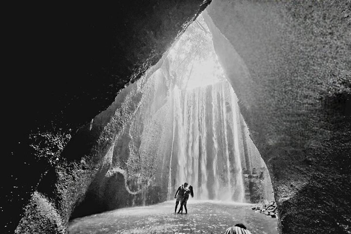 dua orang berdiri di hadapan air terjun