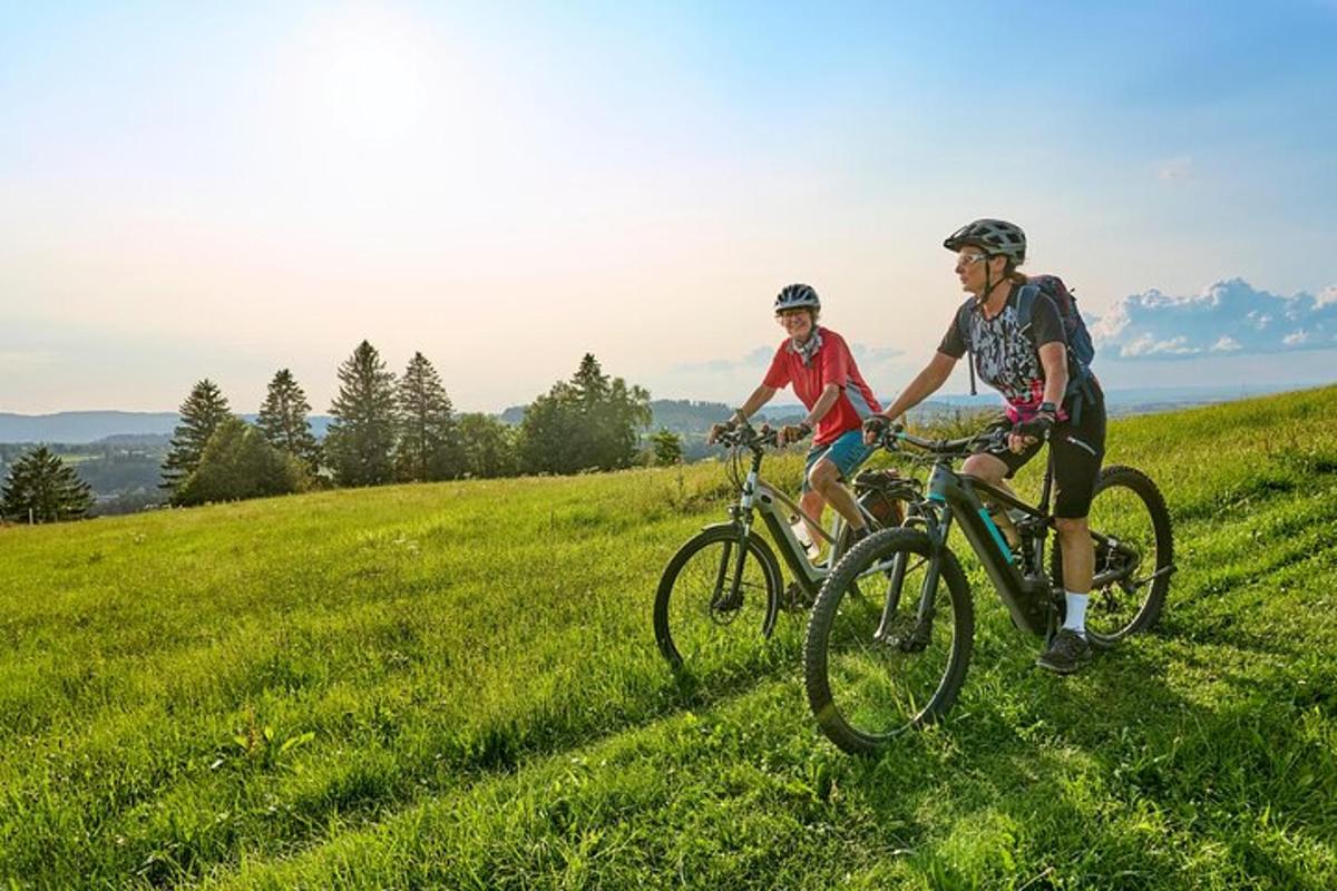 two people riding bikes on a grassy hill