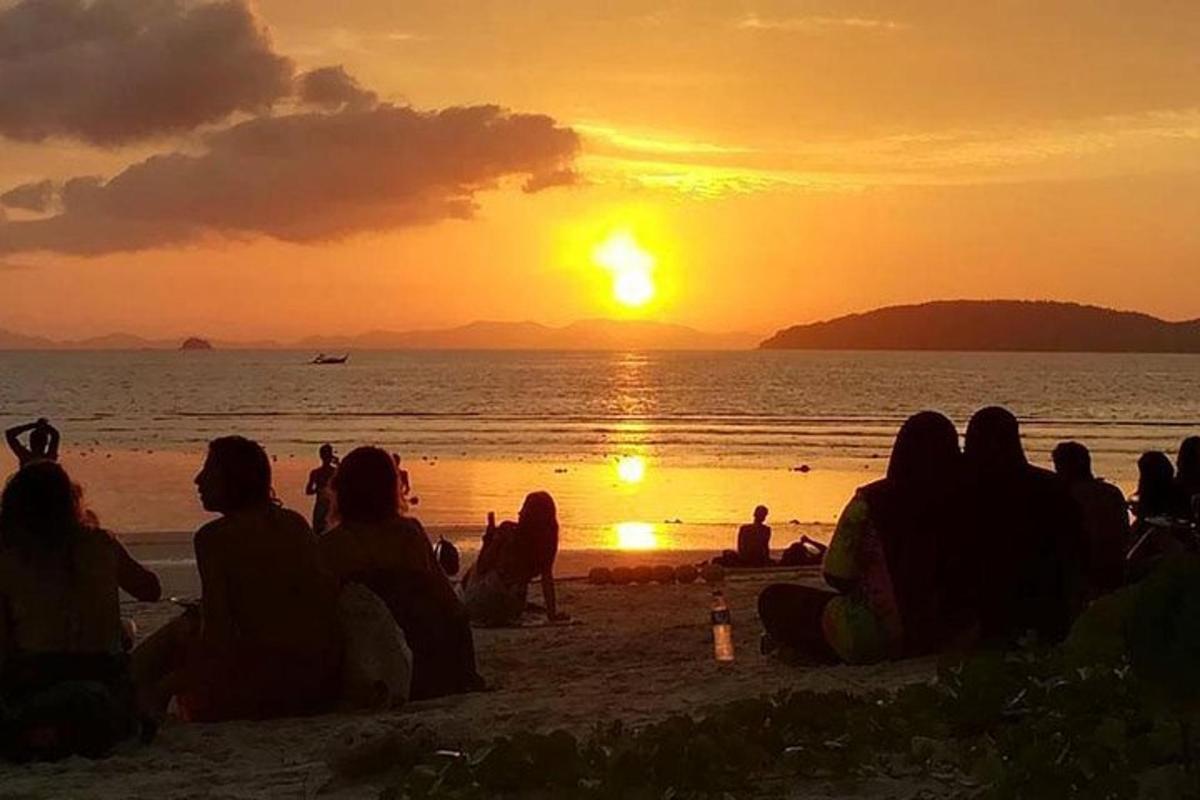 Un grupo de personas sentadas en la playa viendo la puesta de sol