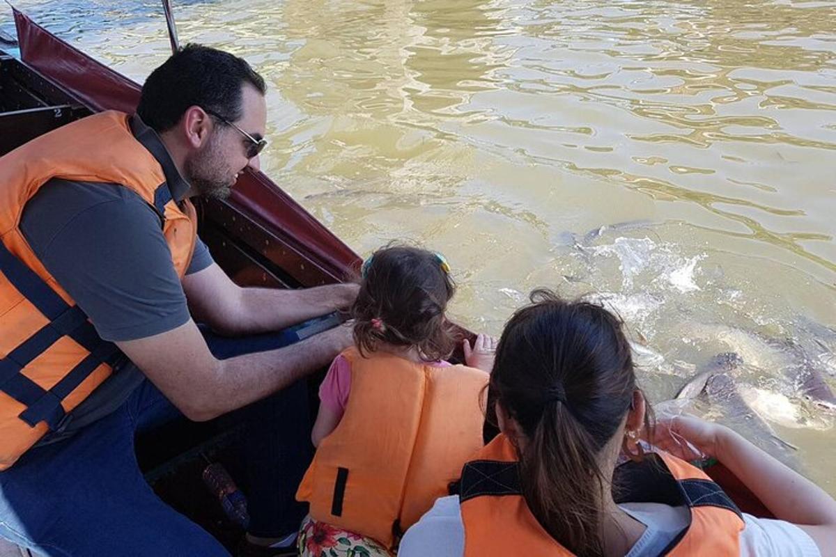 un bărbat și două fete într-o barcă uitându-se la un delfin
