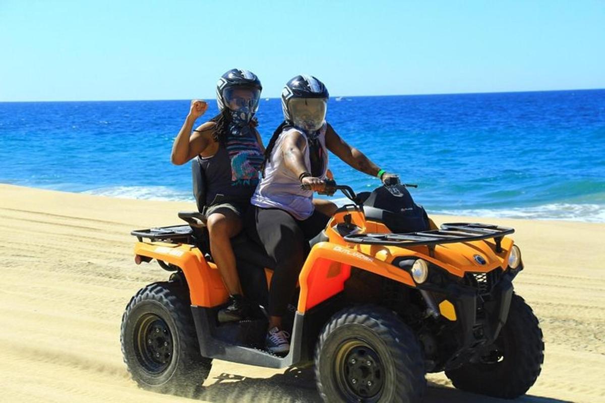 duas pessoas andando em um quadriciclo laranja na praia
