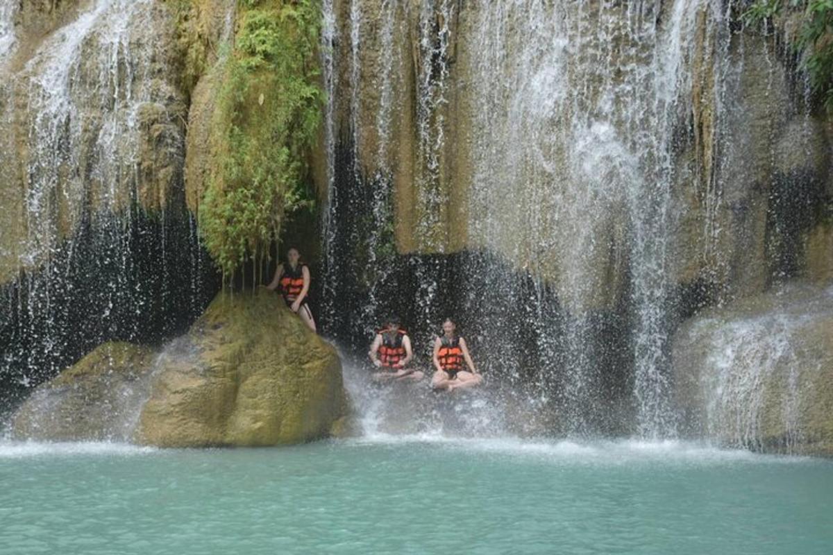 três pessoas sentadas em pedras em frente a uma cachoeira