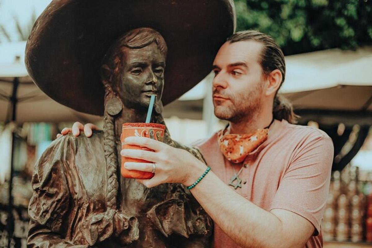 a man holding a drink next to a statue