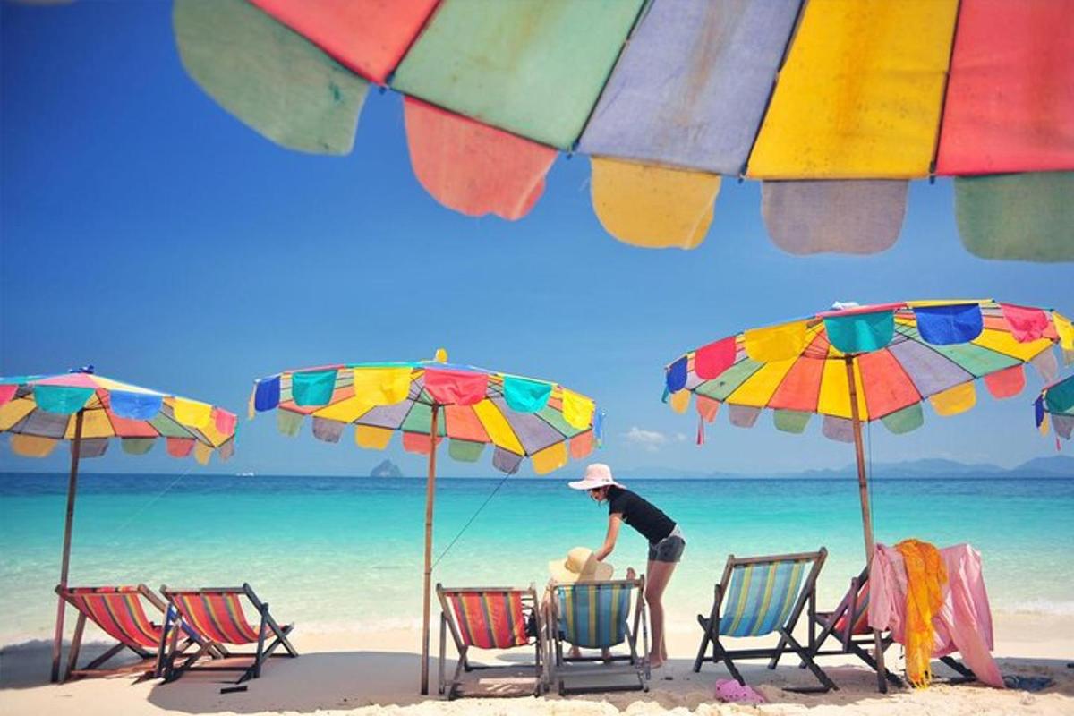 Un hombre parado en una playa con sillas y sombrillas.