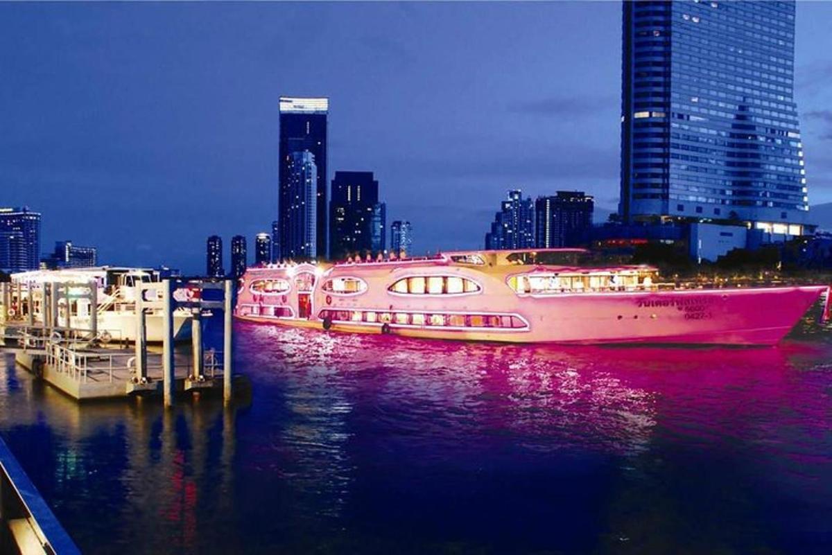 een grote roze boot in het water met een stad