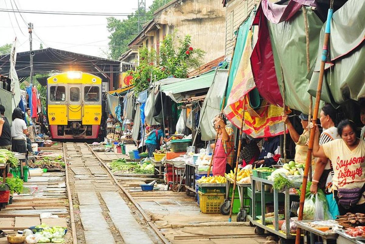một chuyến tàu đang chạy qua một khu chợ có người và rau