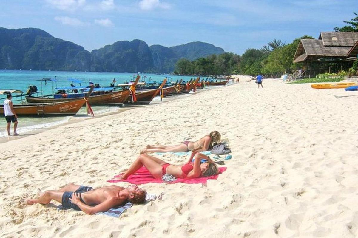 dua orang berbaring di atas tuala di pantai dengan bot