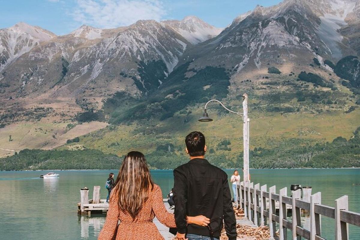 a man and woman standing on a pier looking at a mountain