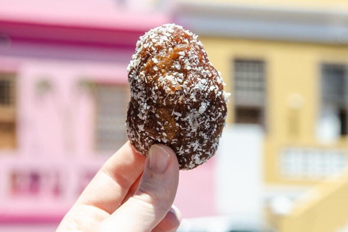 una mano che tiene una ciambella al cioccolato ricoperta di zucchero a velo