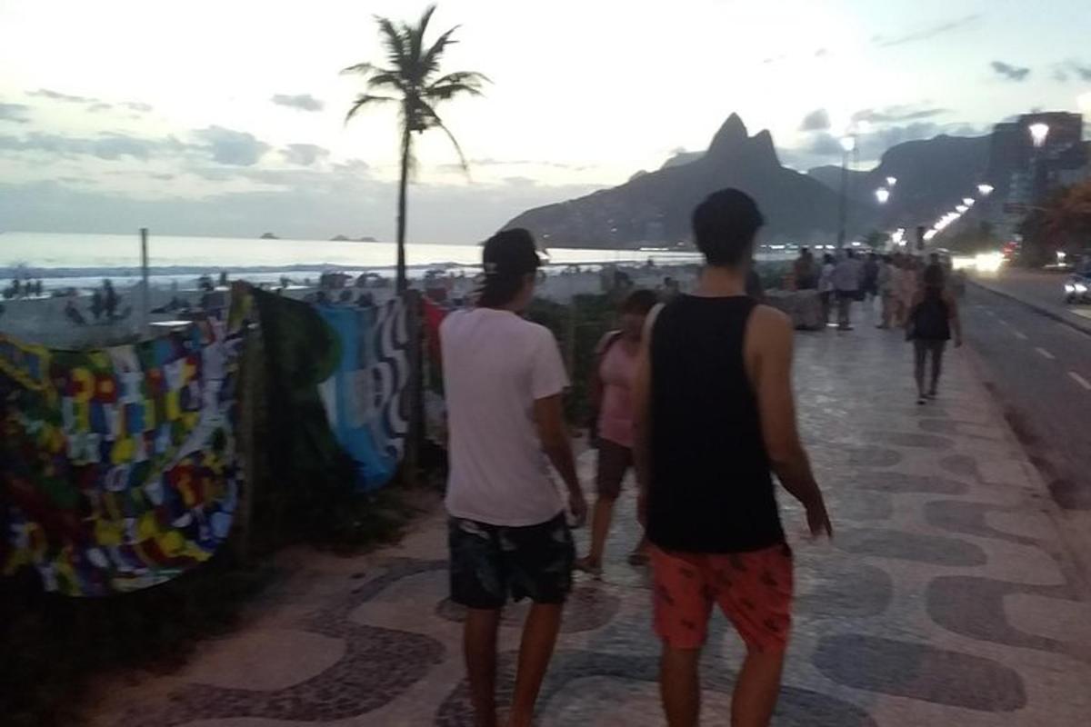 three people walking down a sidewalk near the beach