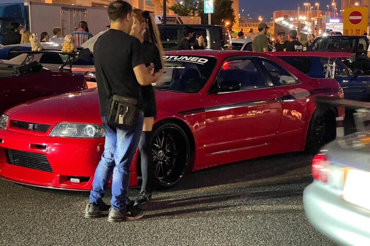 Un hombre y una mujer de pie junto a un coche rojo.