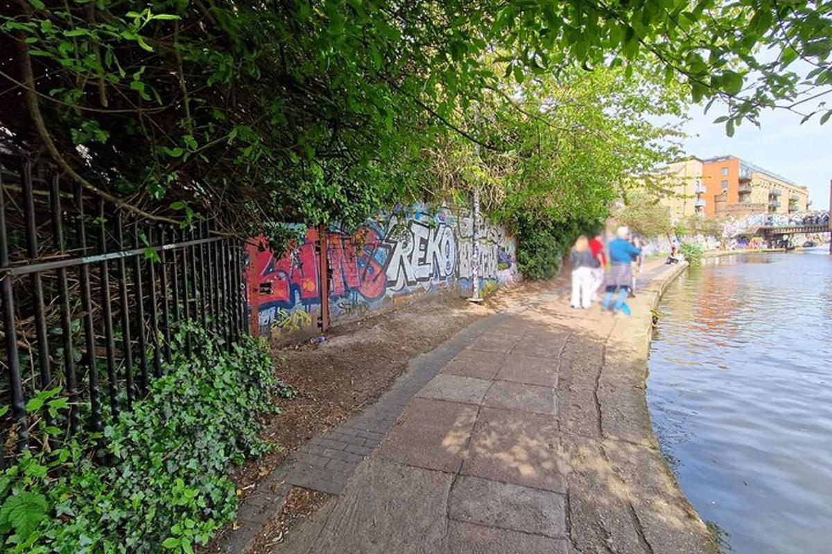dva lidé jdoucí po chodníku vedle řeky s graffiti