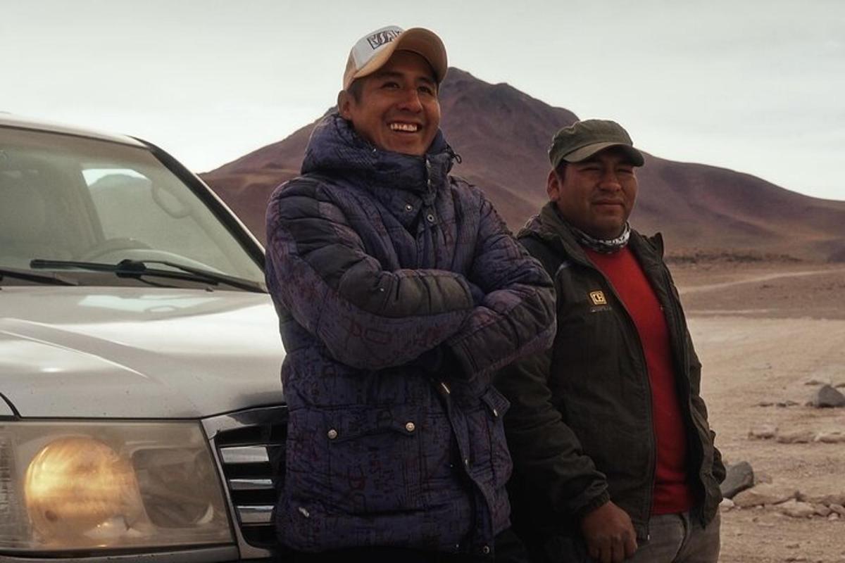 two men standing next to a car in the desert