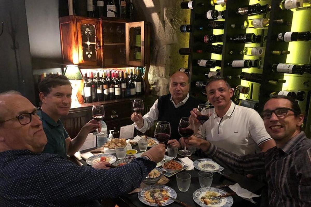 grupė žmonių, sėdinčių prie stalo ir geriančių vyną