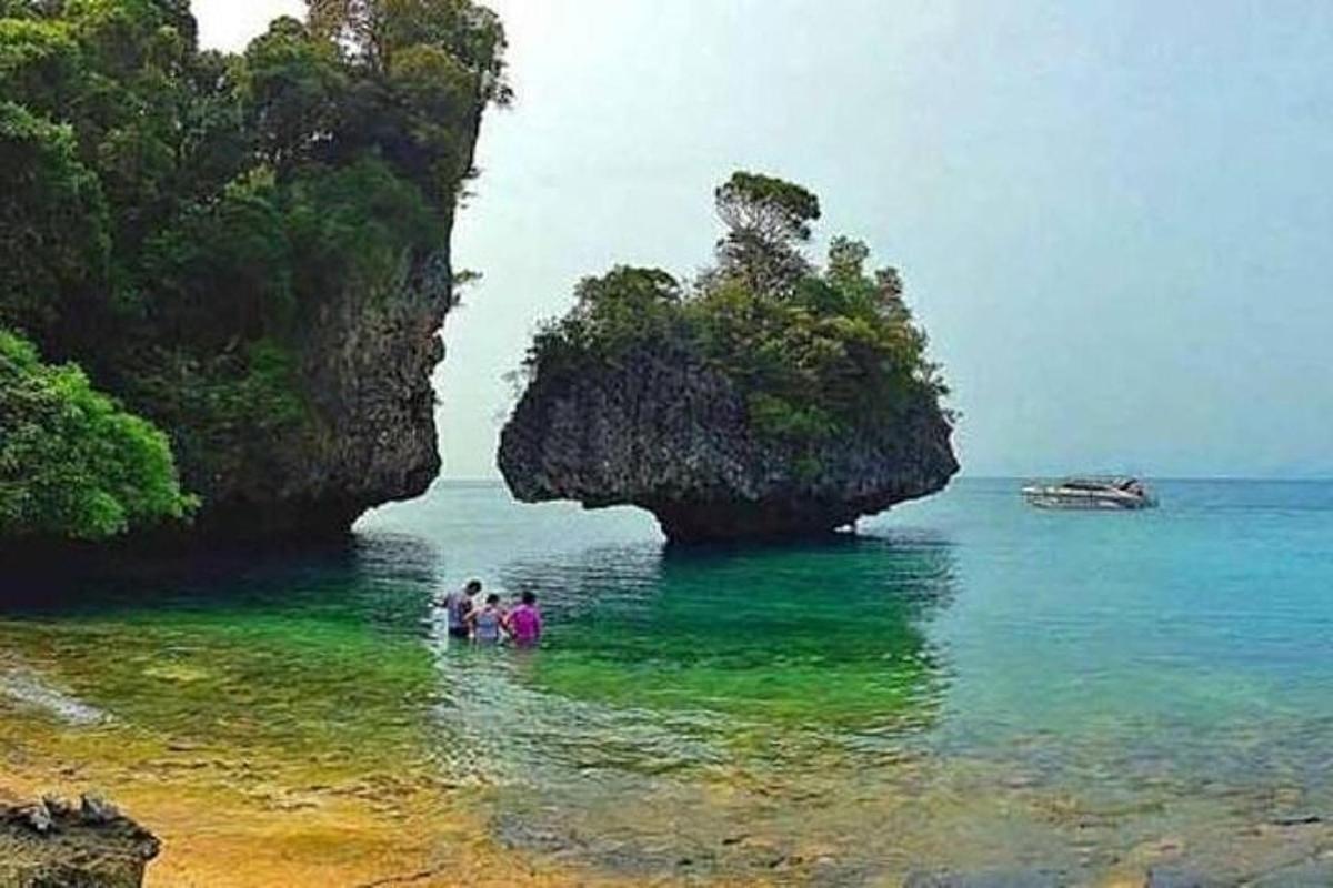 tre persone in piedi nell'acqua vicino a una grotta nell'oceano