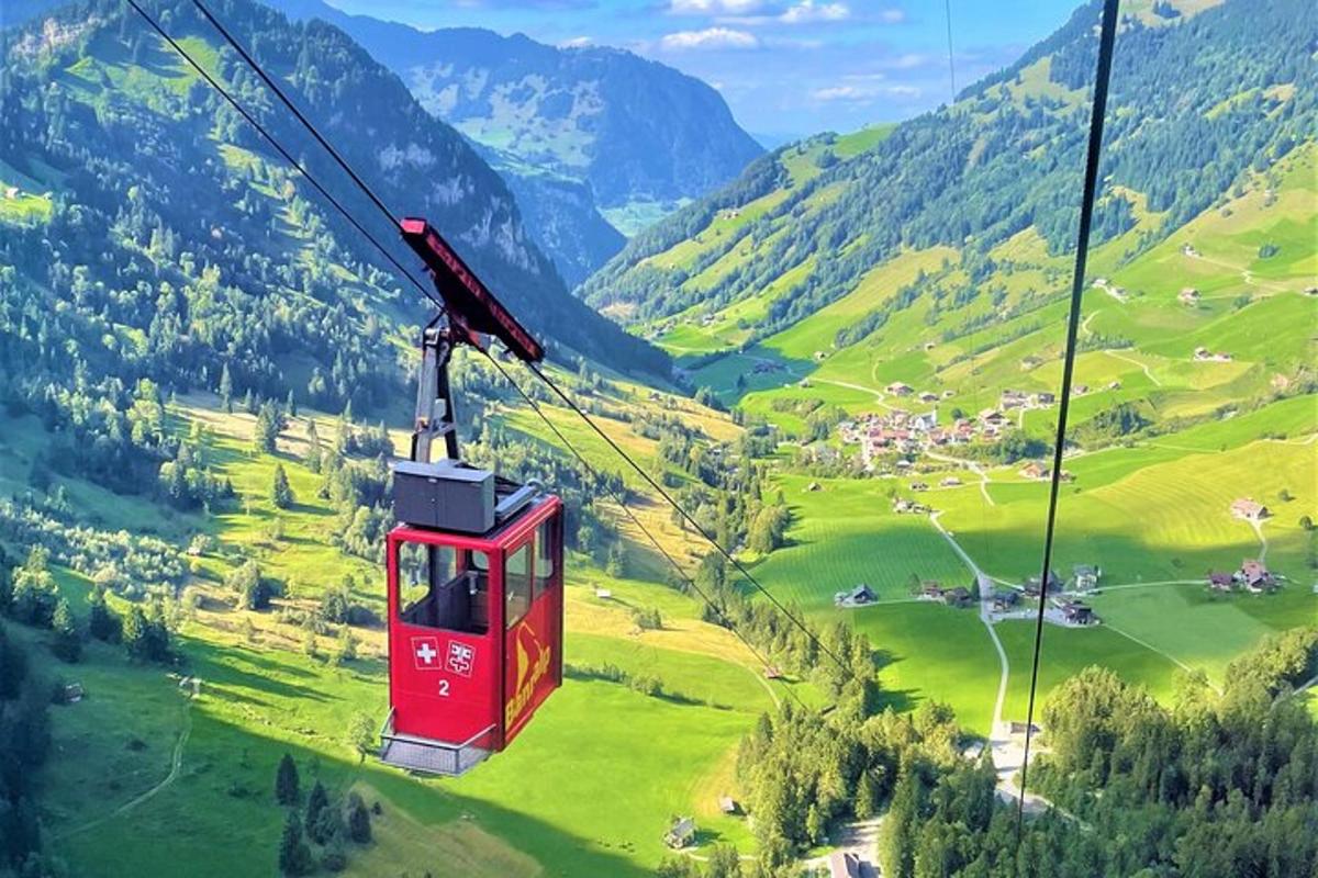 a red gondola flying over a green valley