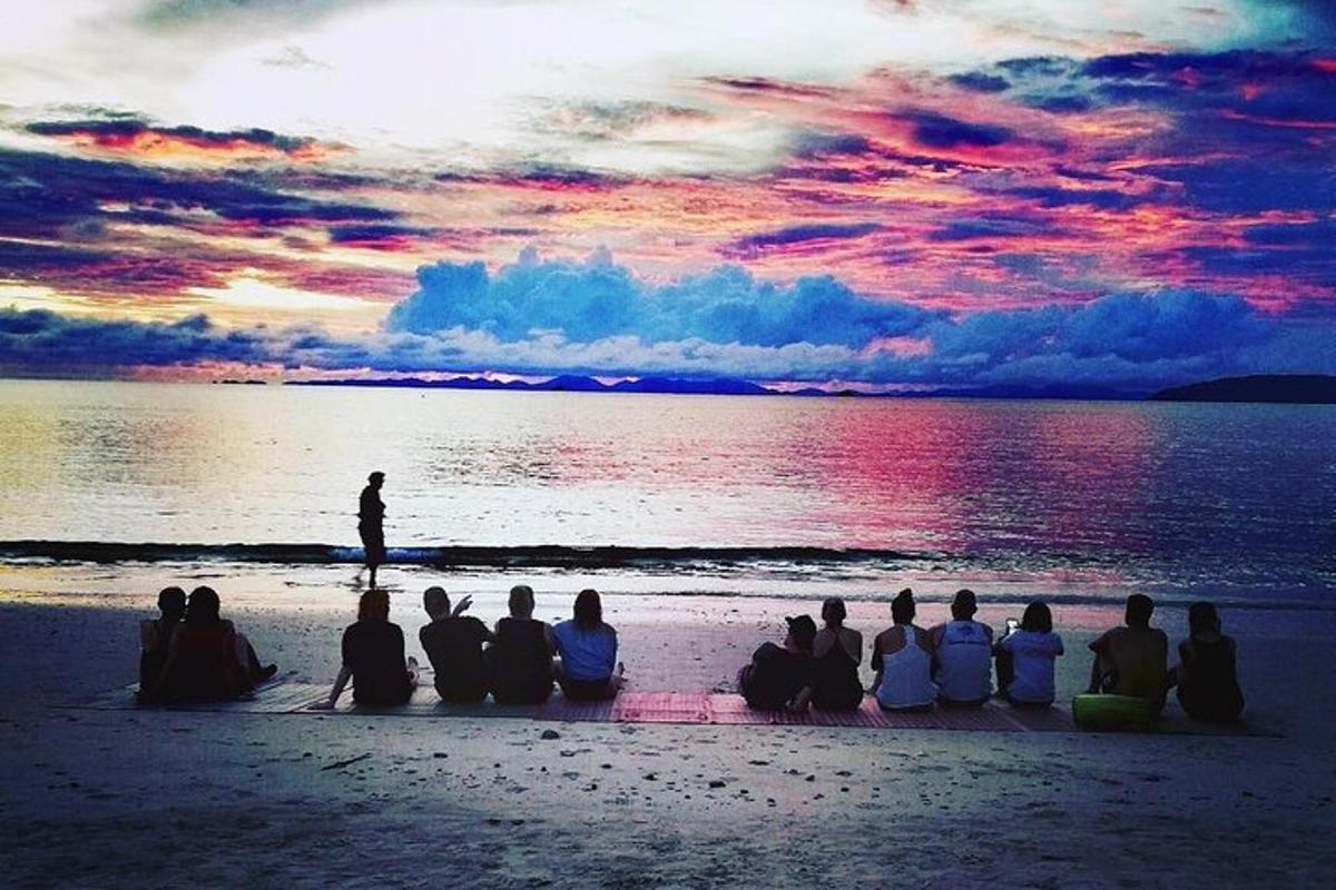 en gruppe mennesker som sitter på stranden og ser på solnedgangen