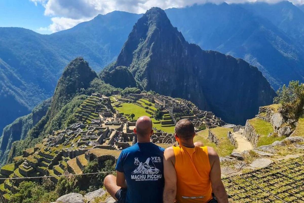 two men sitting on top of a mountain looking at a city
