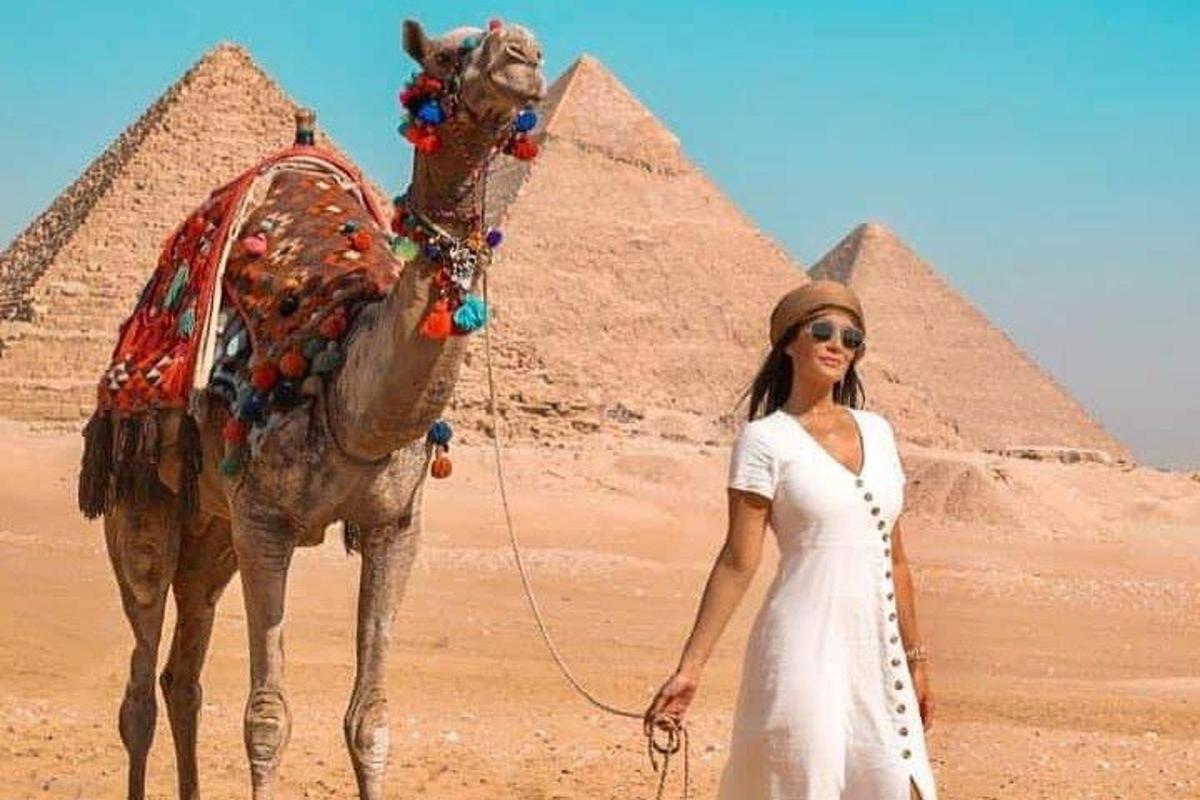 žena stojaca vedľa ťavy pred pyramídami