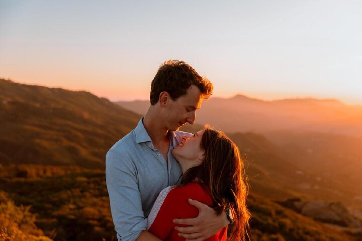 a couple kissing on top of a mountain at sunset