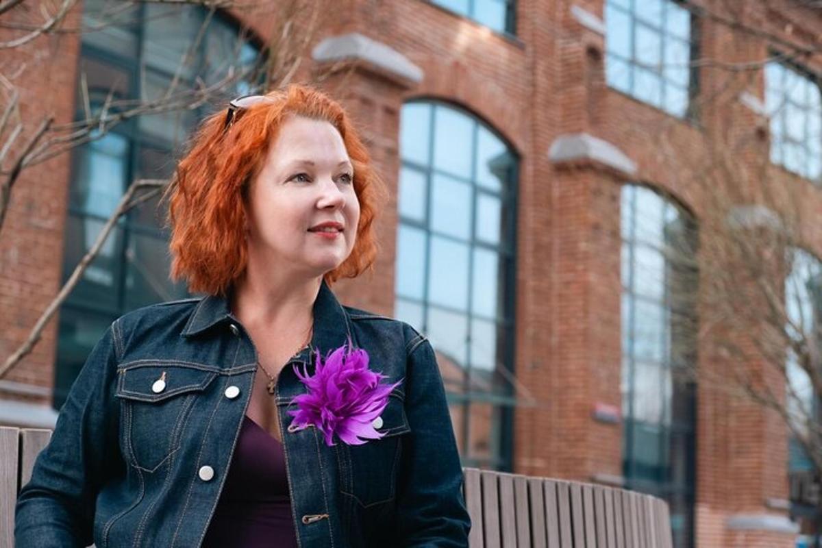 Una mujer pelirroja sosteniendo una flor morada.