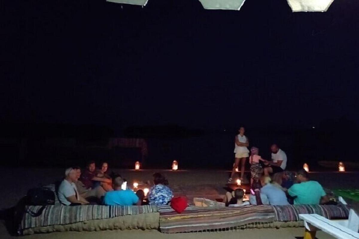 sekumpulan orang yang duduk di pantai pada waktu malam
