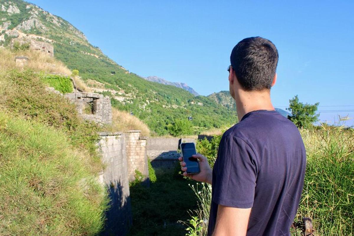 muž držící mobilní telefon, zatímco stojí na kopci