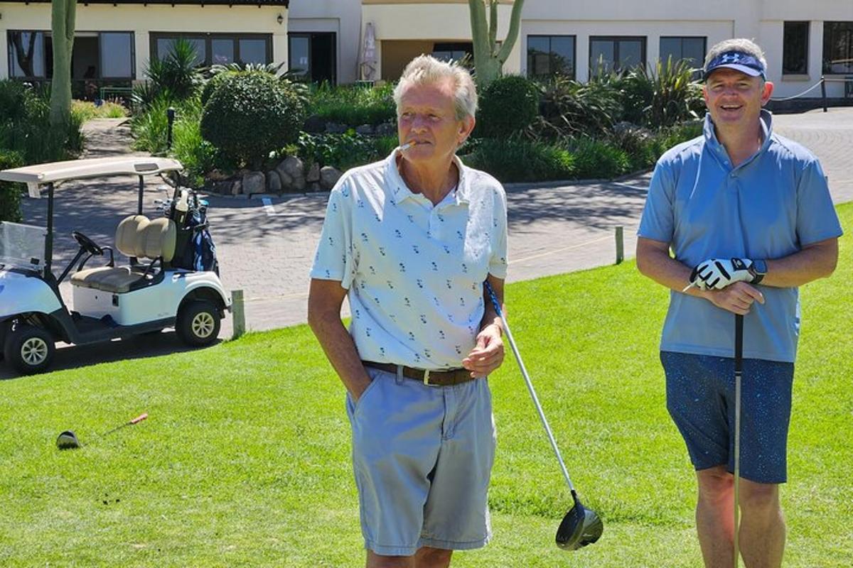 Két idősebb férfi áll a fűben egy golfkocsival