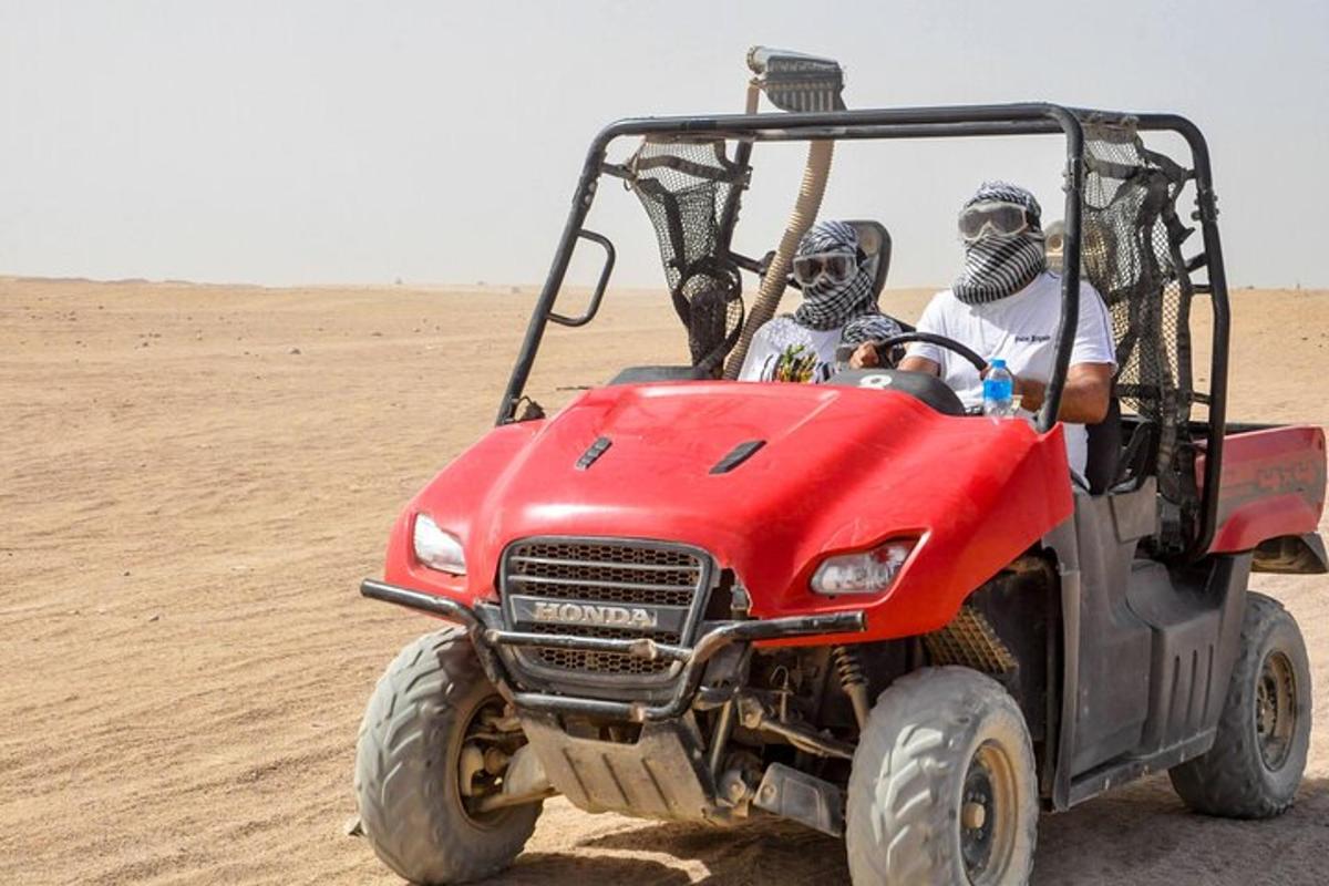 duas pessoas dirigindo um quadriciclo vermelho no deserto