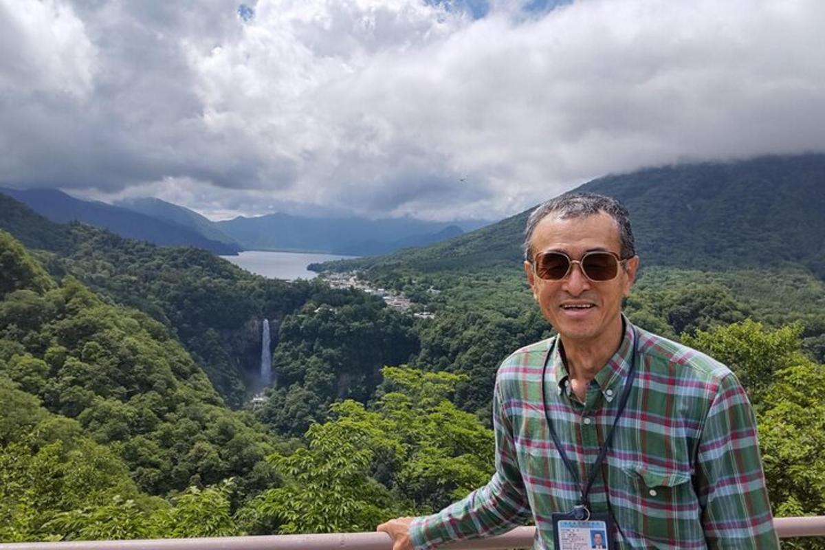 un uomo con occhiali da sole in piedi su una sporgenza con una cascata in lontananza