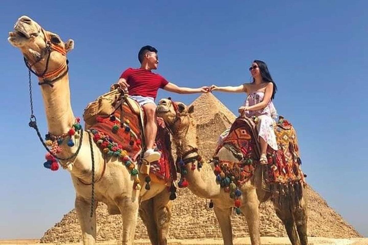 Un hombre y una mujer montados en camellos frente a una pirámide.