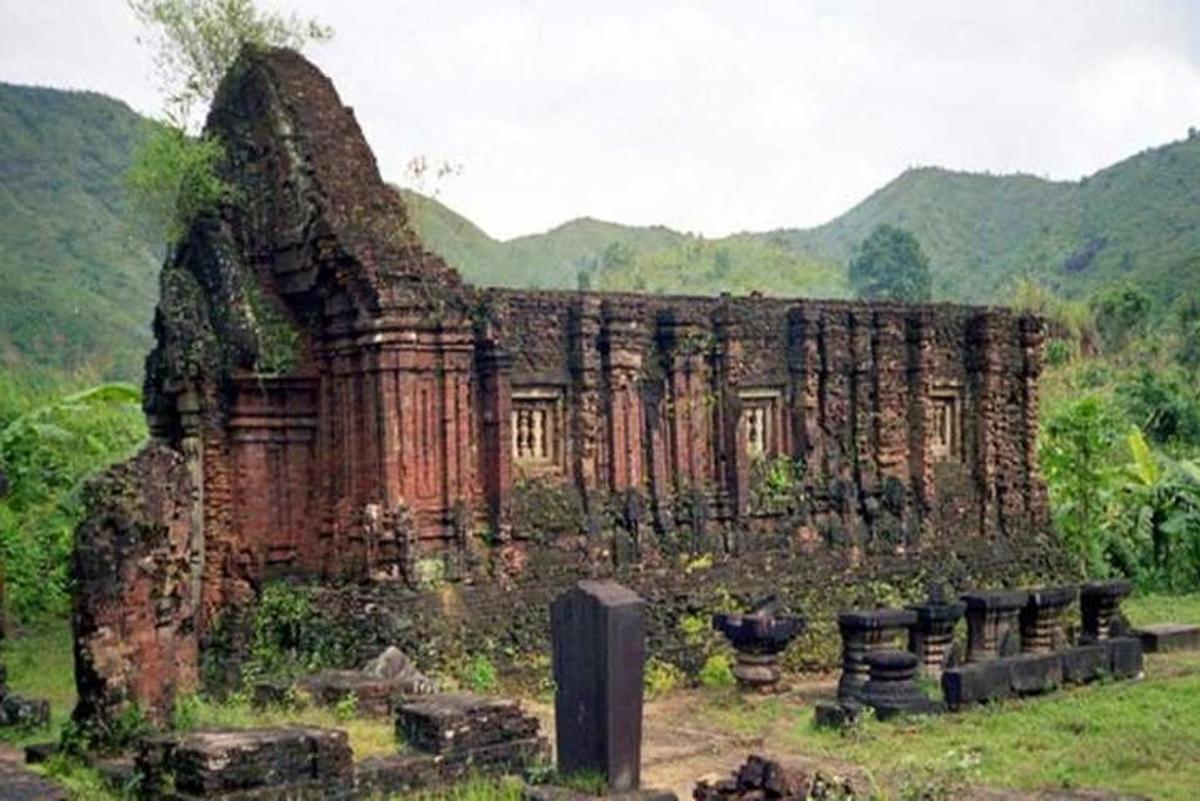 một tòa nhà cũ trên một cánh đồng với những ngọn núi ở phía sau