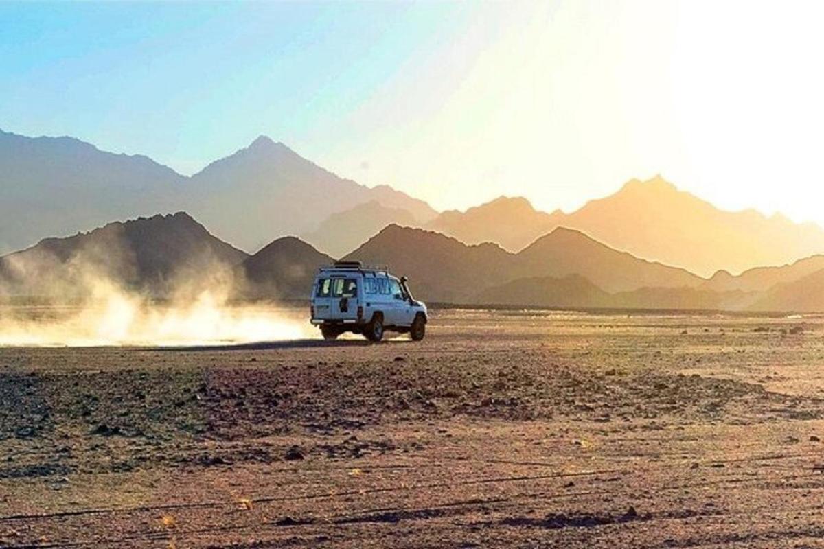 Un vehículo circulando por el desierto con montañas al fondo.
