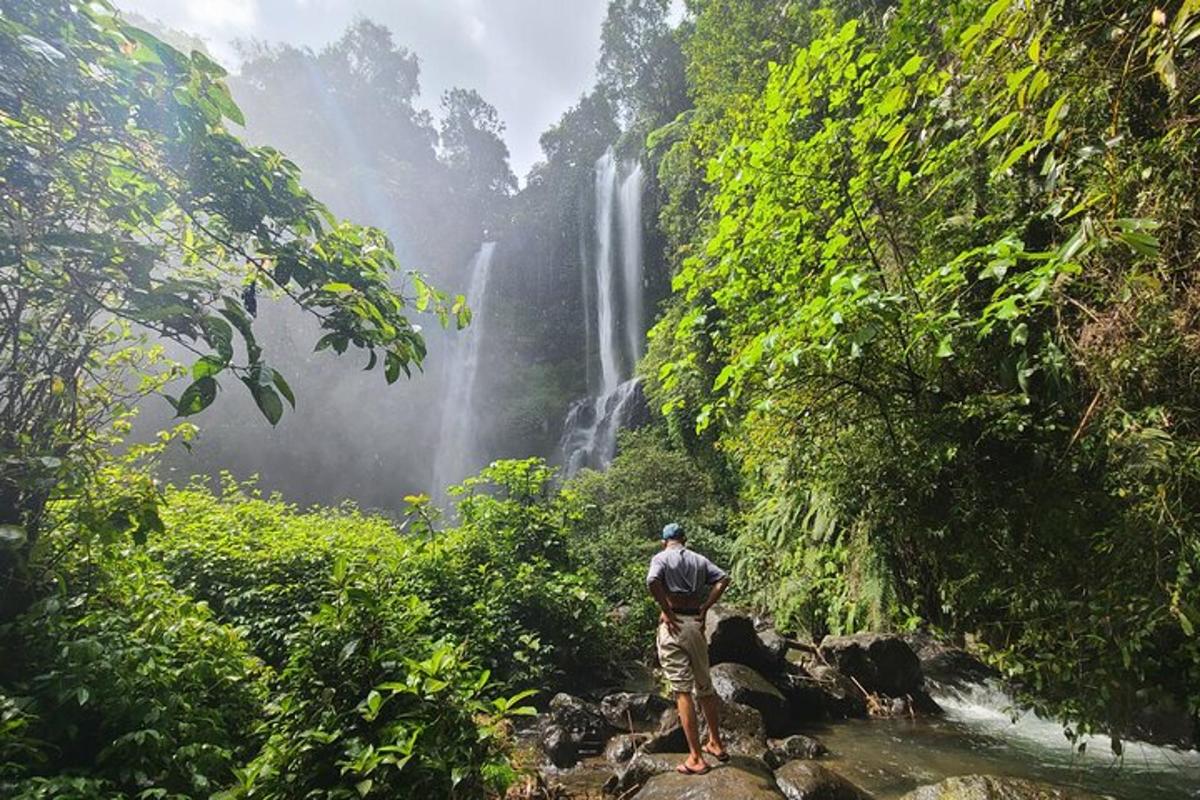 Un hombre parado sobre rocas frente a una cascada.
