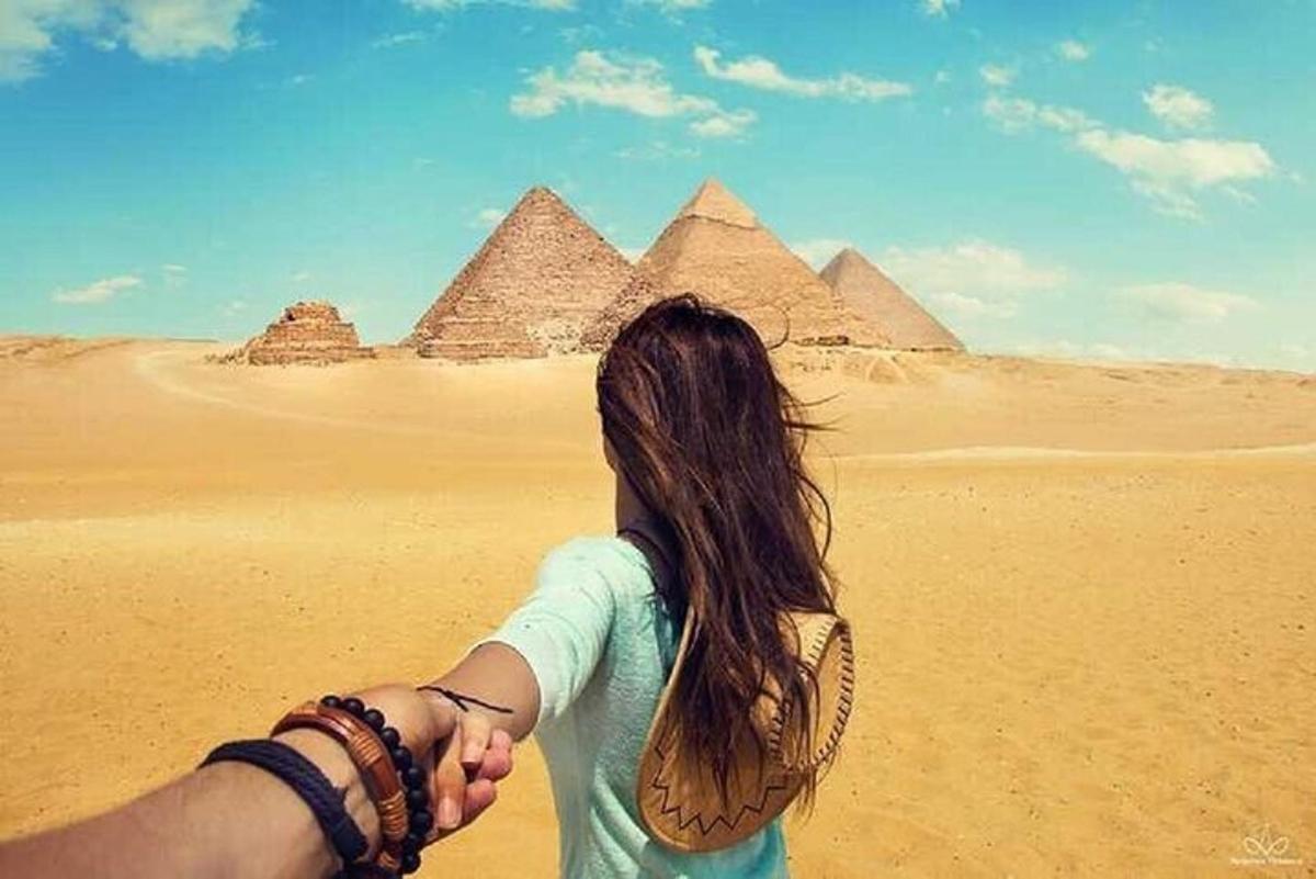 un uomo e una donna che si tengono per mano davanti alle piramidi