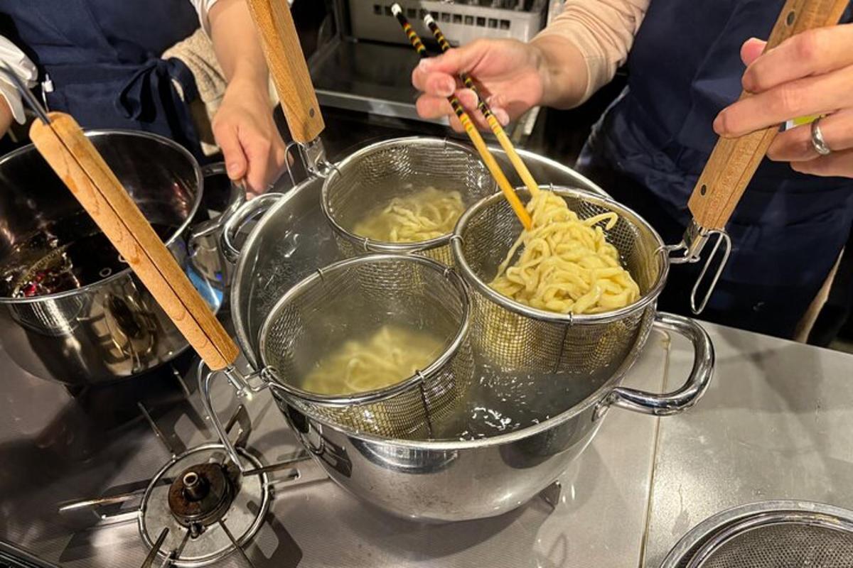 dalawang taong naghahanda ng pansit sa isang kaldero sa isang counter