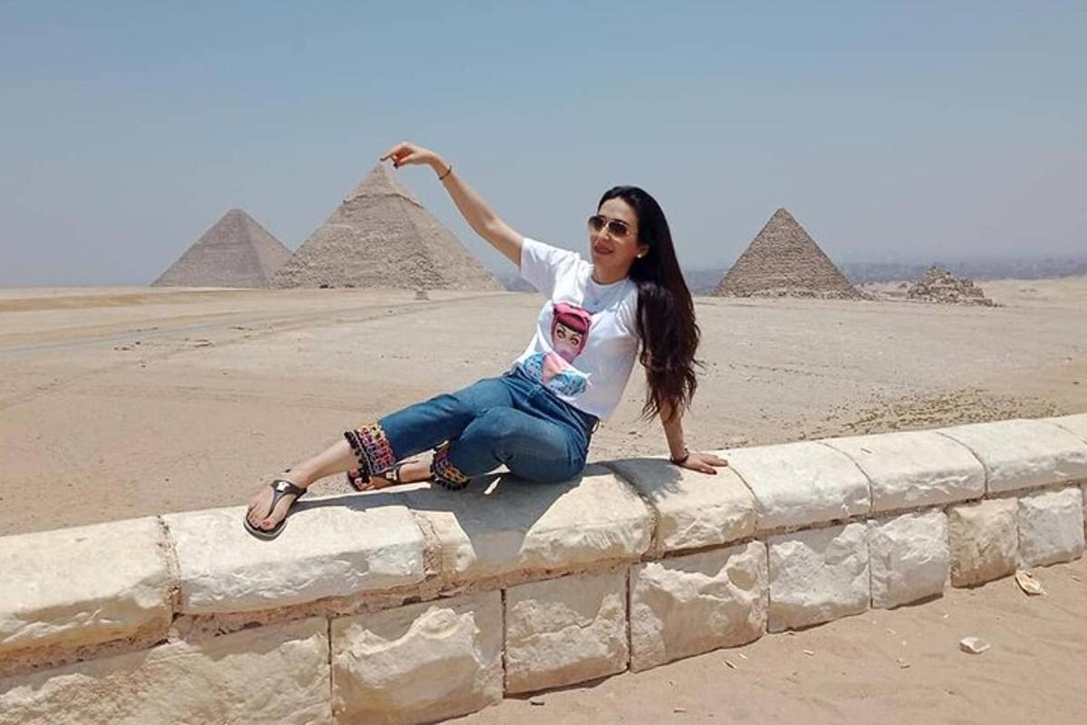 en kvinde sidder på en mur foran pyramider
