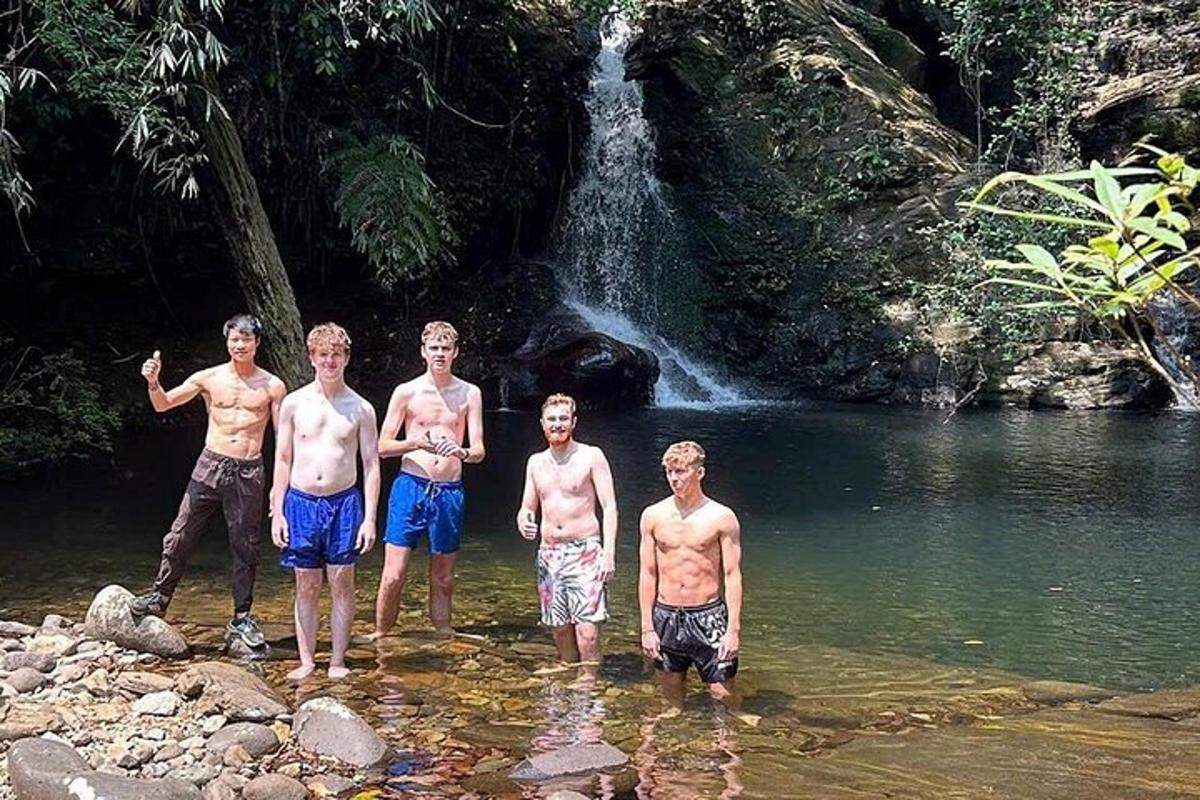 um grupo de meninos parados na água em frente a uma cachoeira