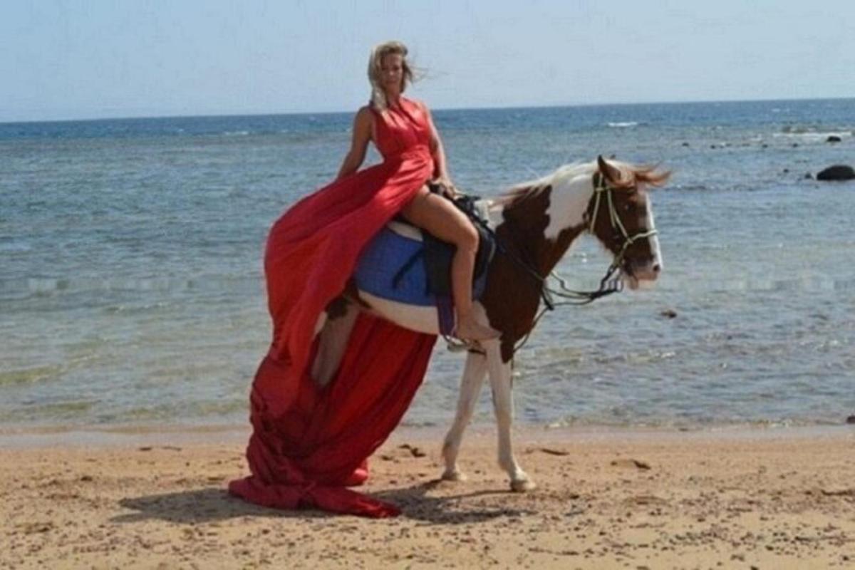 žena v červených šatech jedoucí na koni na pláži