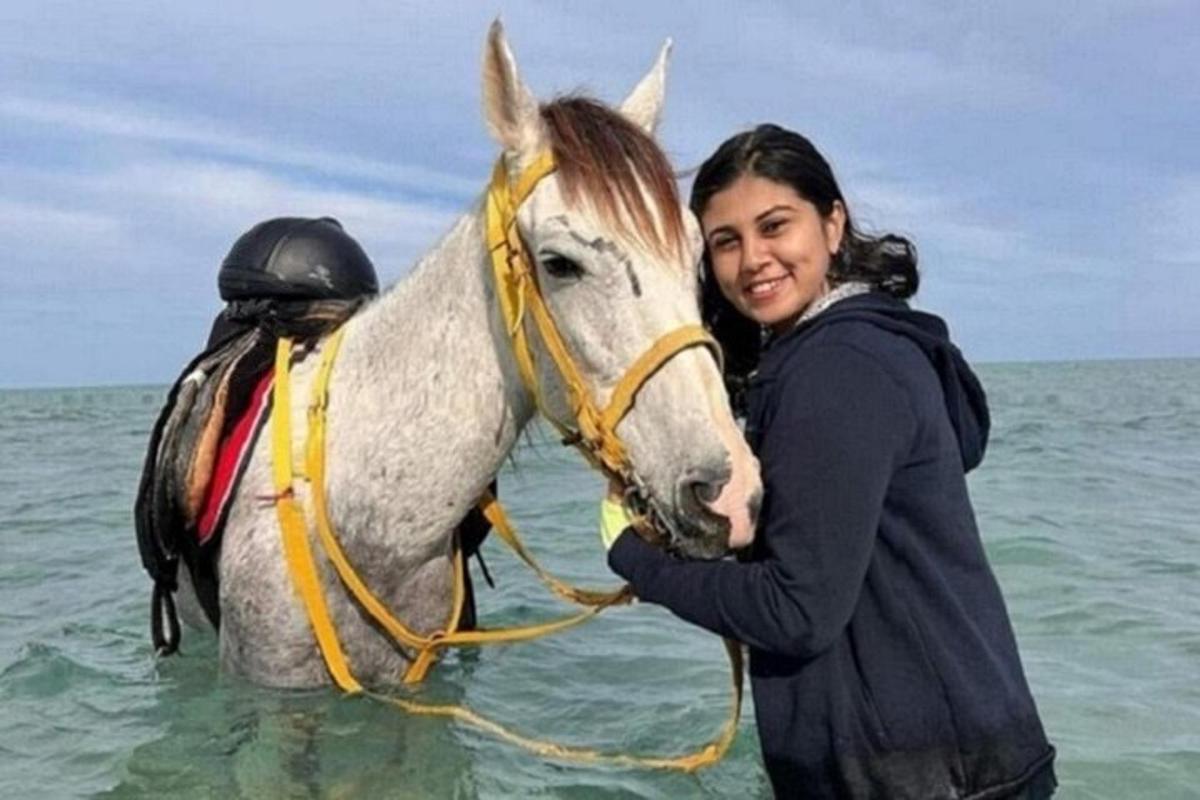una donna in piedi accanto a un cavallo nell'oceano